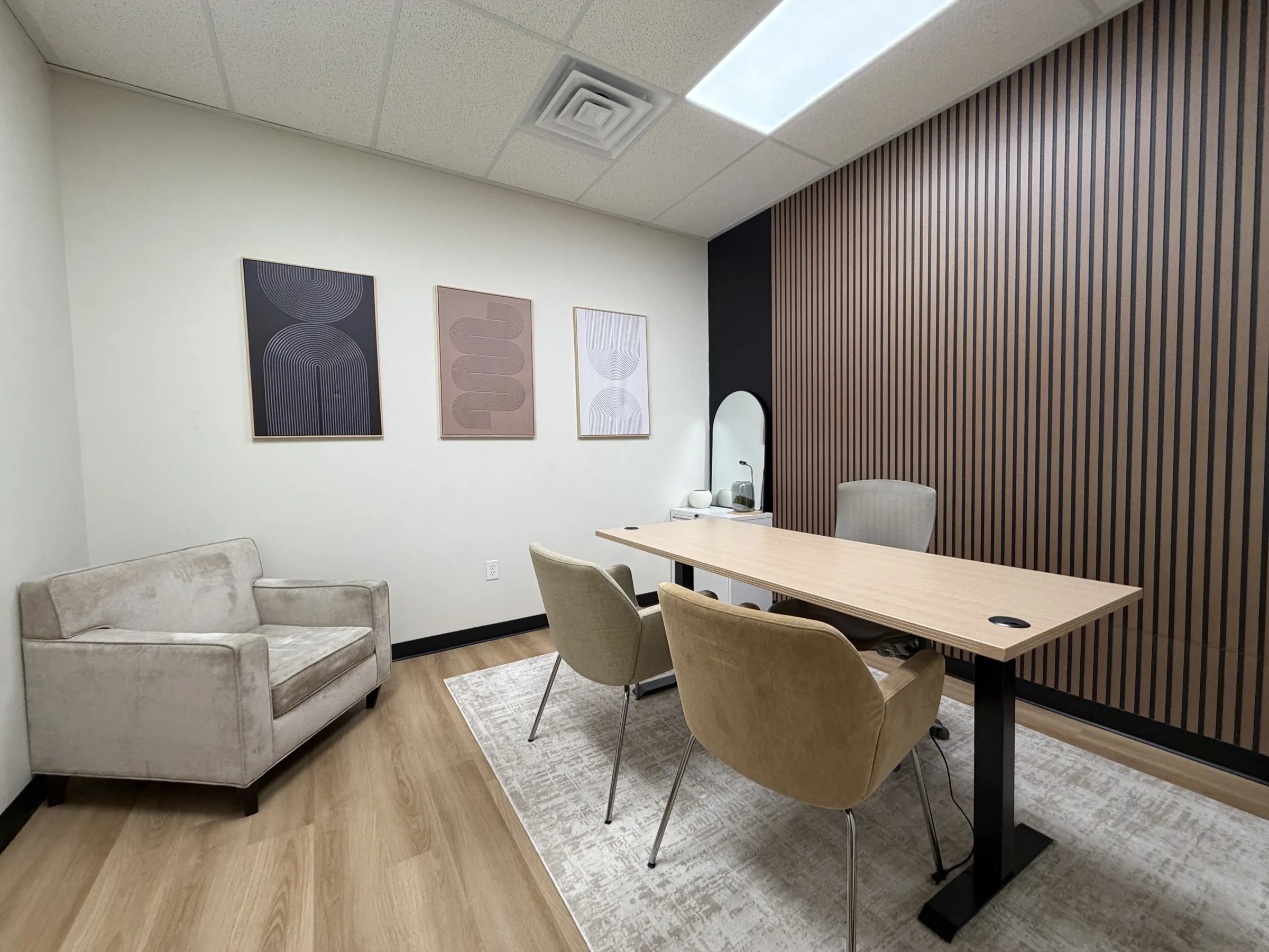 Small furnished meeting office with a desk, guest chairs, a loveseat, and wood slat accent wall
