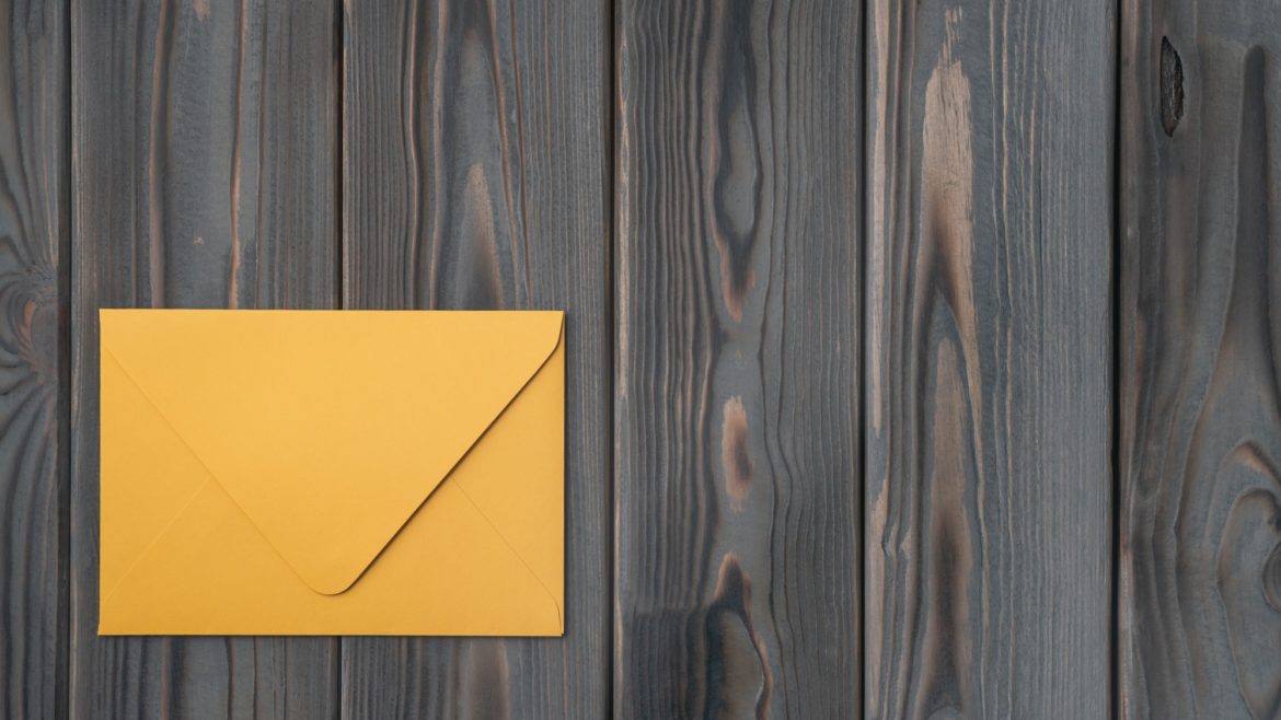 Flat lay of yellow closed envelope on grey wooden table. Correspondence, mailing, post office