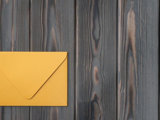 Flat lay of yellow closed envelope on grey wooden table. Correspondence, mailing, post office
